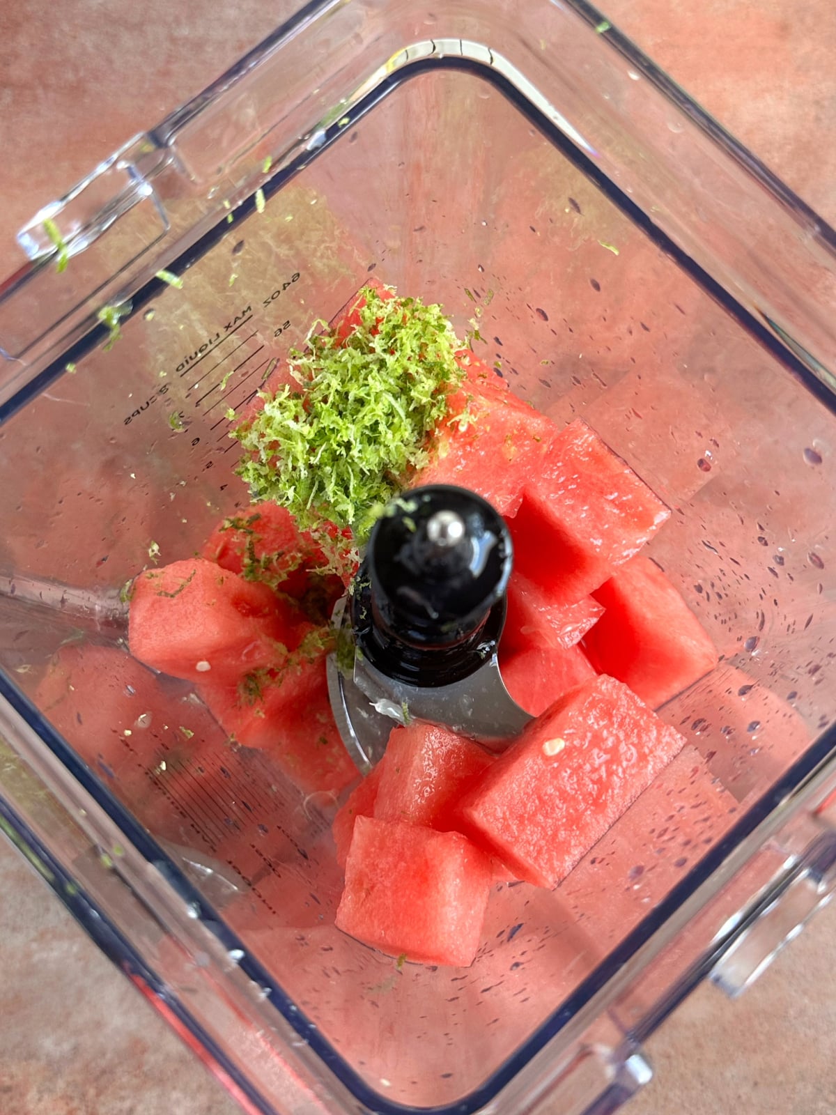 A blender cup filled with chunks of watermelon, club soda, and lime zest.