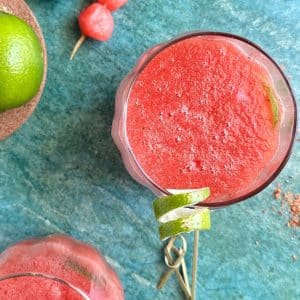 An overhead shot of a glass of watermelon refresher mocktail, with a twisted lime slice on the side.