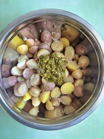 A mixing bowl filled with cooked baby potatoes with seasonings and chimichurri sauce on top.