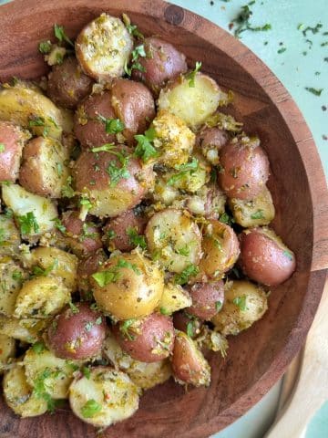 A wooden bowl containing Chimichurri potato salad with serving utensils on the side.