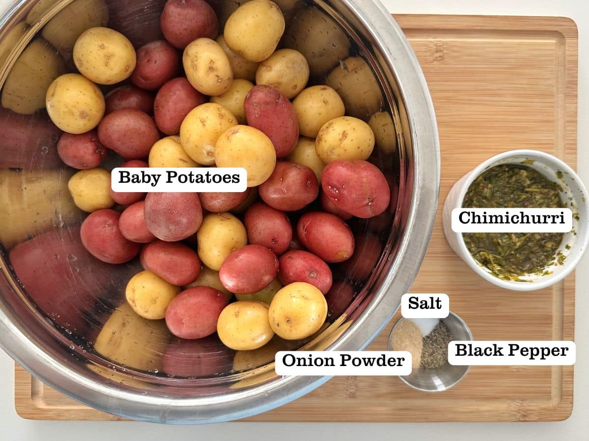A wooden board containing bowls of ingredients for chimichurri potato salad.
