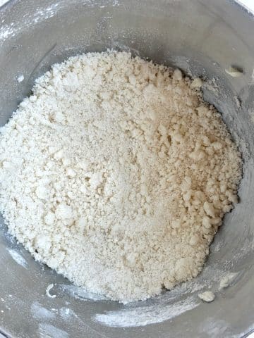 A mixing bowl with butter and flour combined into a sandy texture.