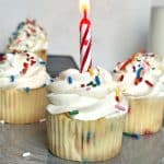 A shot of homemade confetti cupcakes with a lit candle sticking inside one of them.