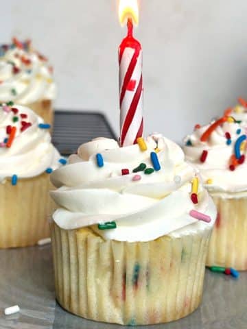 A shot of homemade confetti cupcakes with a lit candle sticking inside one of them.