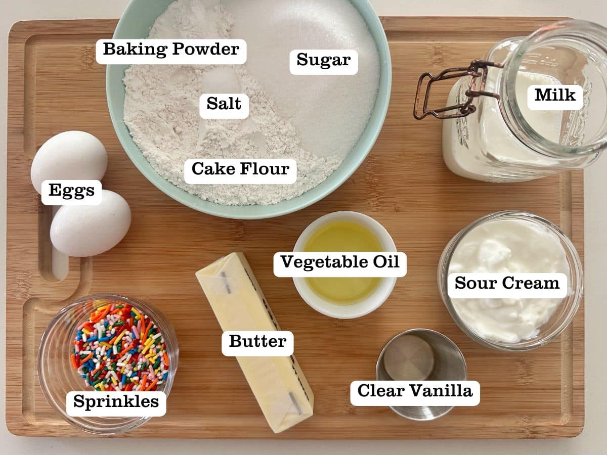A wooden board with bowls of ingredients for confetti sprinkle cupcakes.