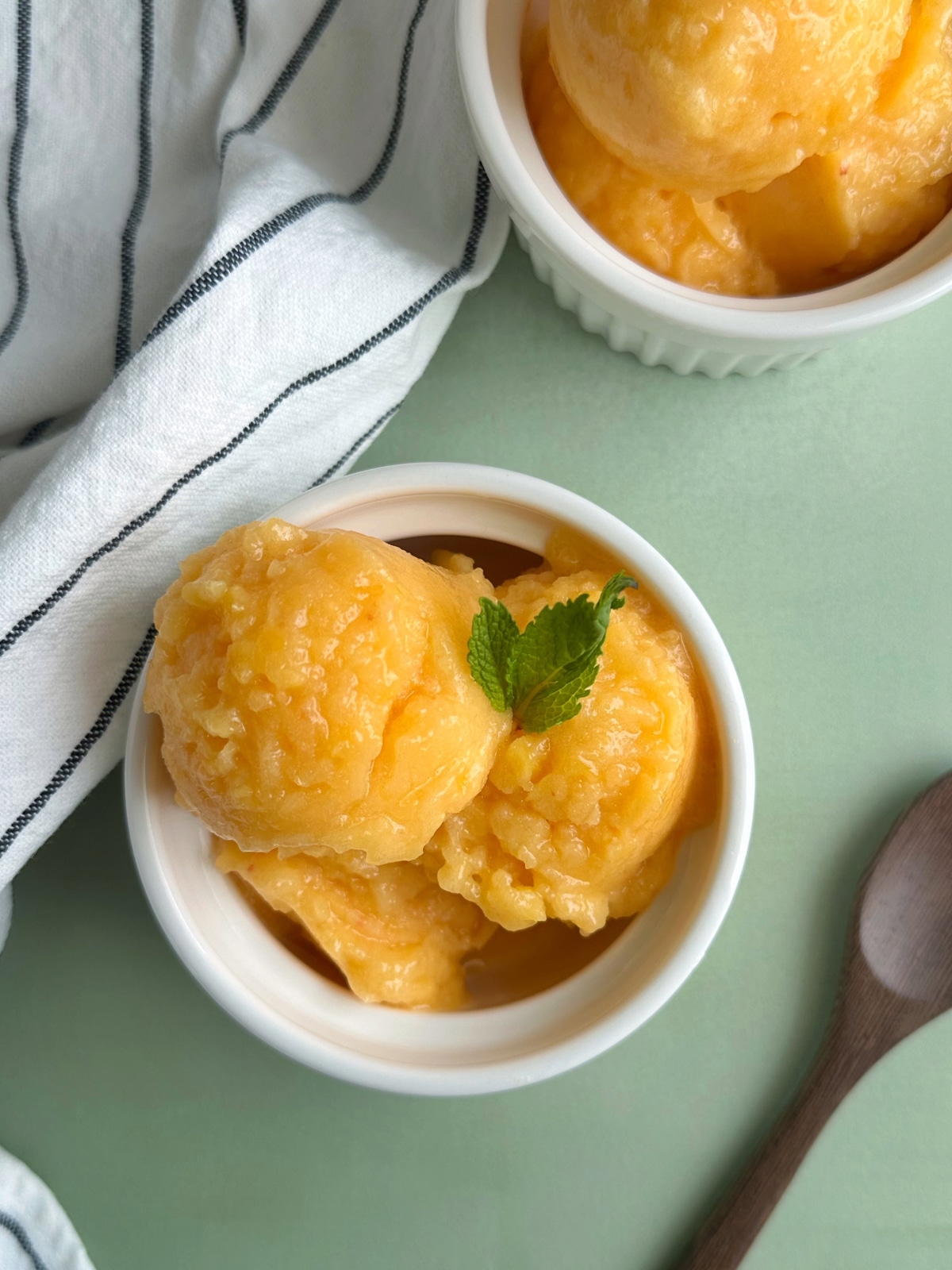 Two bowls of peach ginger sorbet with mint leaves on top.