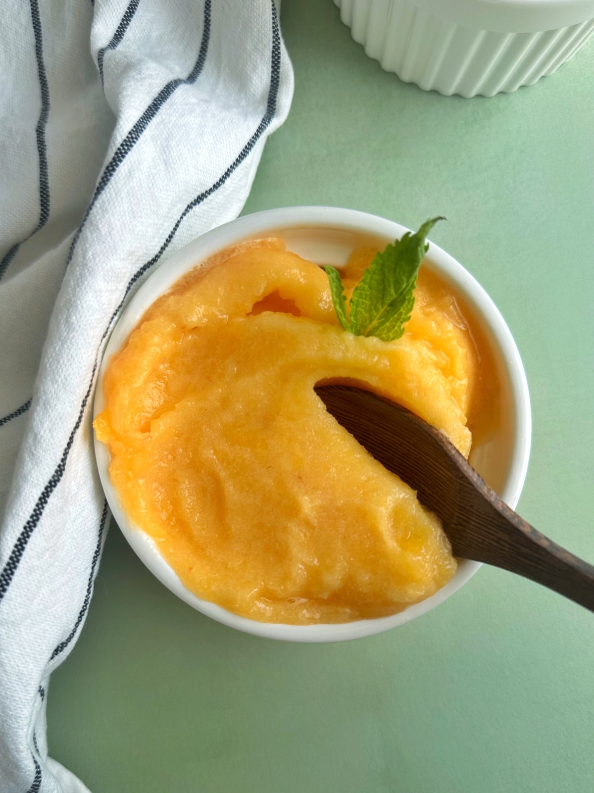 A wooden spoon stuck inside a bowl of peach ginger sorbet.