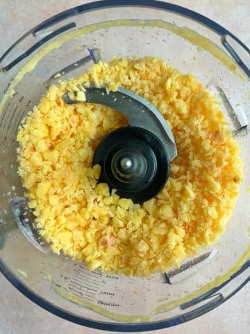 A food processor with pieces of blended frozen peaches.