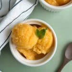 A bowl filled with scoops of peach ginger sorbet with mint leaves on top.