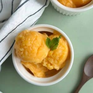 A bowl filled with scoops of peach ginger sorbet with mint leaves on top.