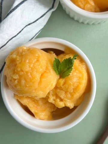 A bowl filled with scoops of peach ginger sorbet with mint leaves on top.