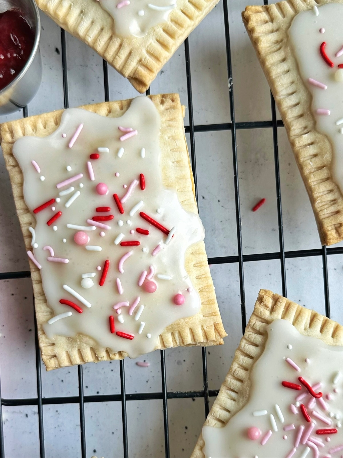 A closeup shot of a homemade strawberry toaster pastry with white icing and pink and red sprinkles.