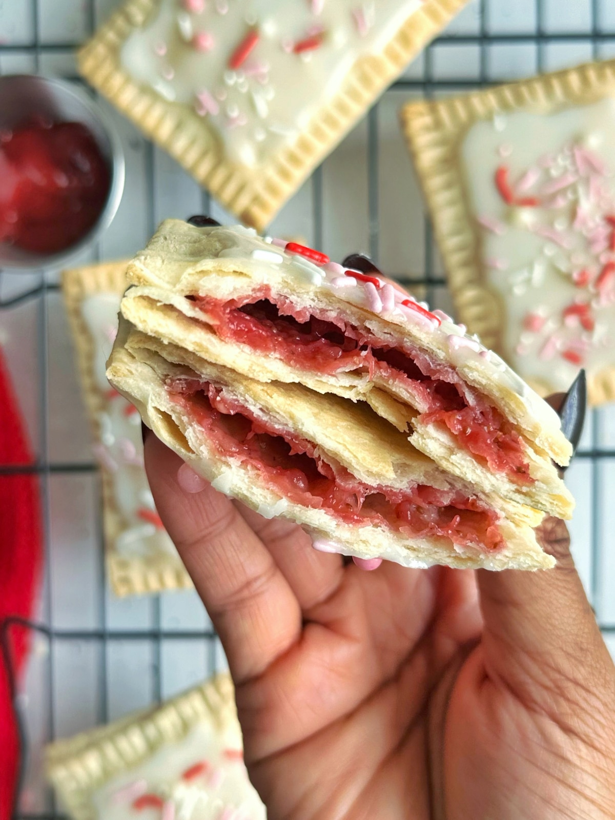 A hand holding two pieces of strawberry pop tarts over a wire rack filled with more.