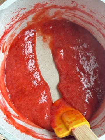 Strawberry jam in a pot with a silicone spoon pulling a line through the middle.