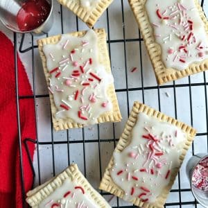 Homemade strawberry pop tarts with red and pink sprinkles on a wire rack.