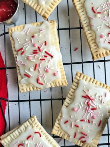 Homemade strawberry pop tarts with red and pink sprinkles on a wire rack.