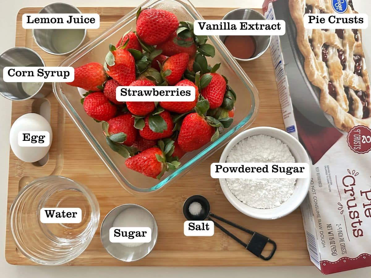 A wooden board containing bowls of ingredients to make homemade strawberry pop tarts, including berries, sugar, and lemon juice.