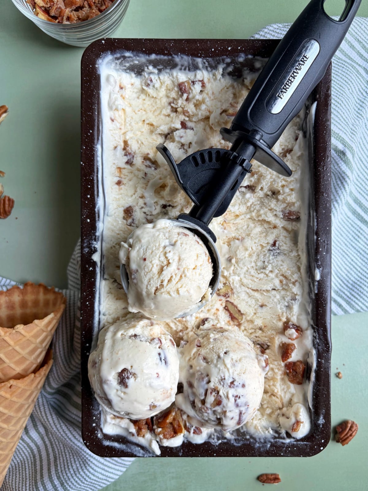 A loaf pan filled with no churn butter pecan ice cream, with scoops sitting on top.