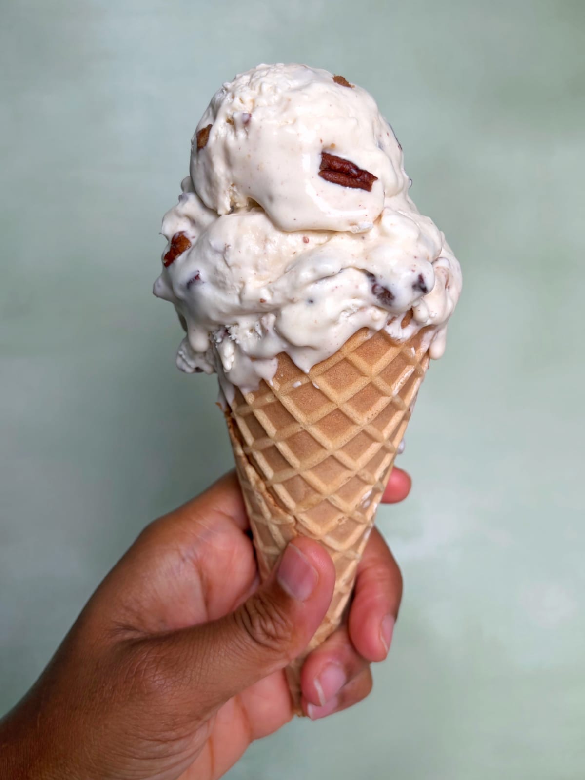 A hand holding a waffle cone with three scoops of butter pecan ice cream.