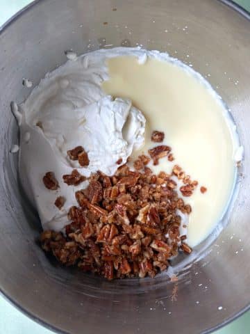 A mixing bowl with praline pecans, whipped cream, and sweetened condensed milk.