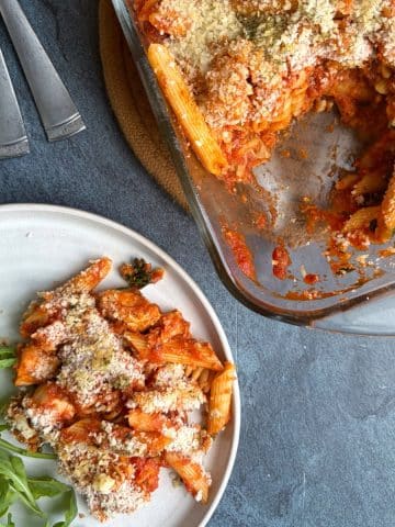 A plate of chicken parmesan pasta bake next to the pan with the rest of the dish inside.