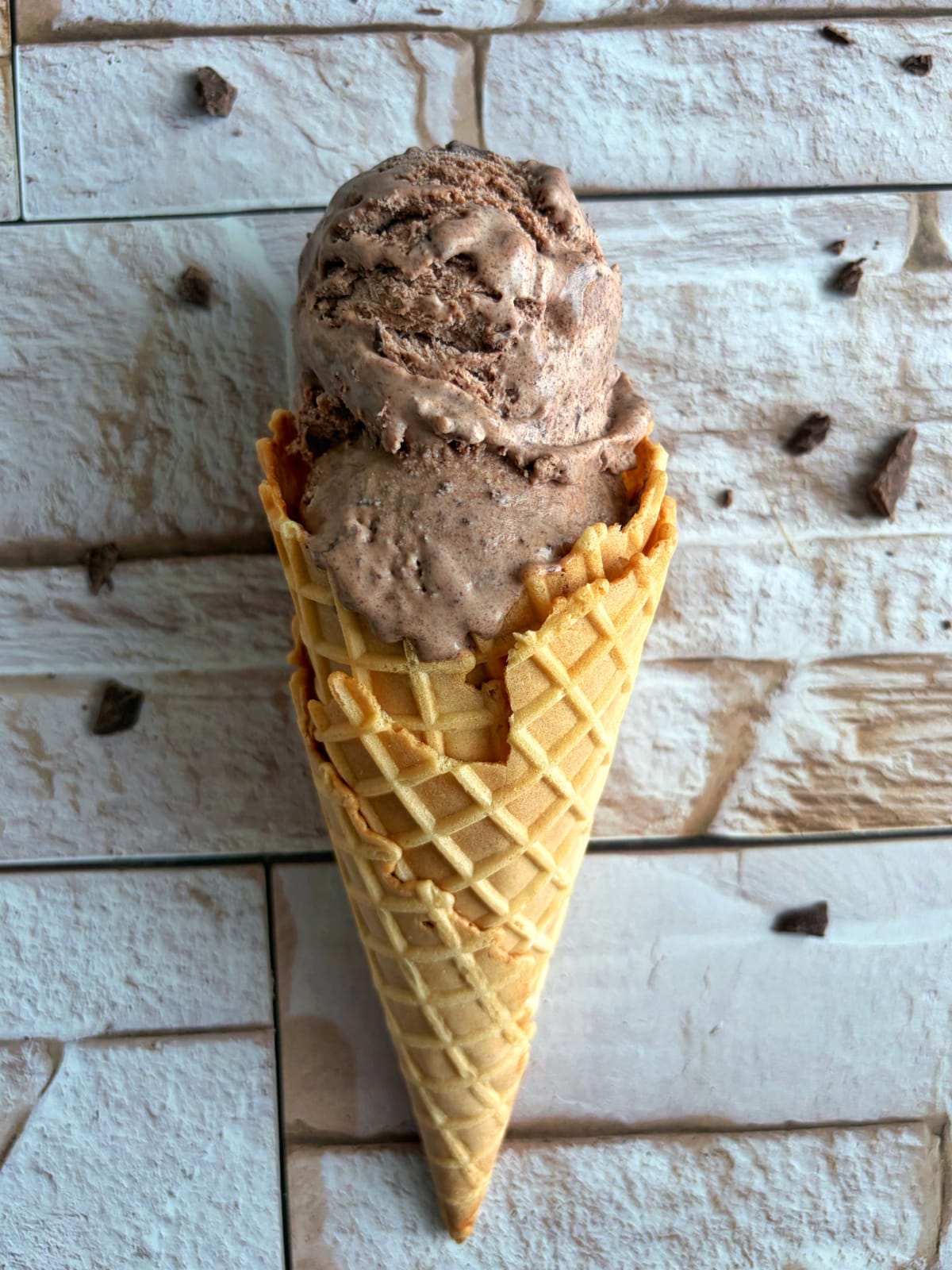 An ice cream cone with two scoops of dark chocolate ice cream.