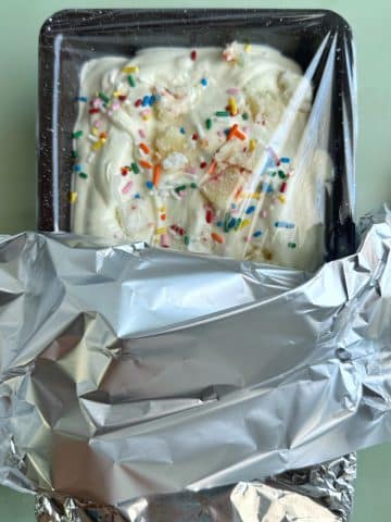 A loaf pan filled with no-churn ice cream, wrapped in plastic wrap and aluminum foil.