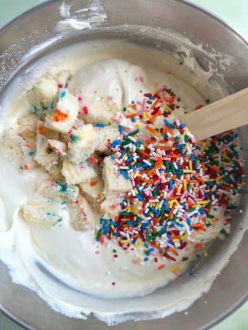 A bowl of vanilla ice cream base with cake pieces and rainbow sprinkles inside.