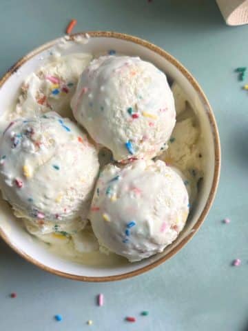 A bowl with three scoops of birthday cake funfetti ice cream inside.