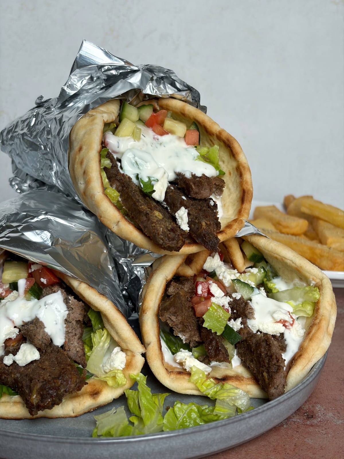 A stack of 3 foil-wrapped gyro wraps with lamb and vegetables inside.