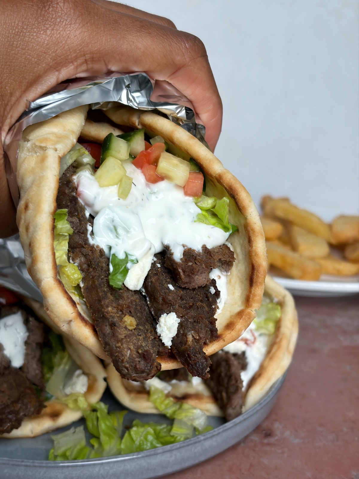 A hand holding out a lamb gyro with tzatziki, wrapped in foil.