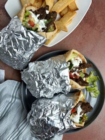 A shot of aluminum foil-wrapped gyros with fries on the side.