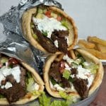 A stack of three lamb gyro wraps with fries on a plate in the background.