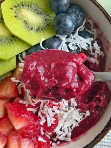 A spoon scooping up a bite of blueberry smoothie bowl.