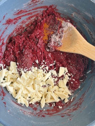 Chopped white chocolate in a mixing bowl with red velvet cookie dough.