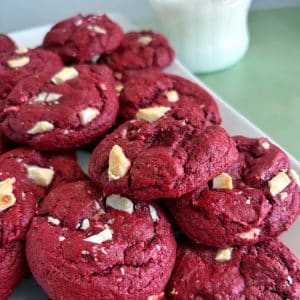 A stack of red velvet cake mix cookies on a plate with a glass of milk in the background.