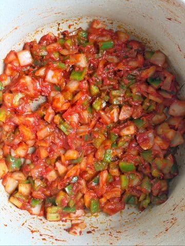 A pot filled with sautéed chopped onions, peppers, and tomato paste.