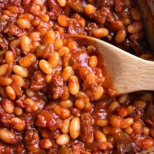 A pot of southern baked beans with a wooden spoon scooping up some of them.