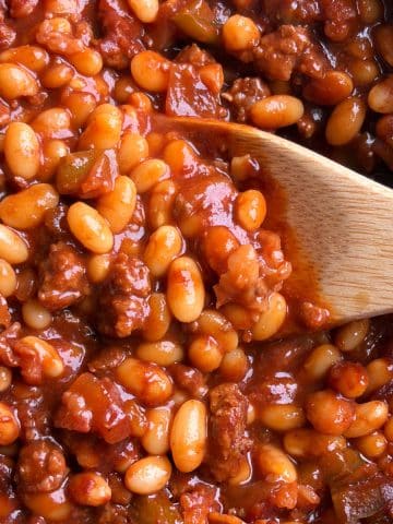 A pot of southern baked beans with a wooden spoon scooping up some of them.