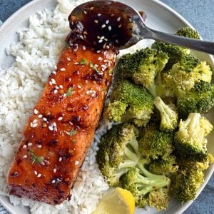 A plate of rice, broccoli, and honey soy salmon with a spoon pouring on more of the sauce on top.