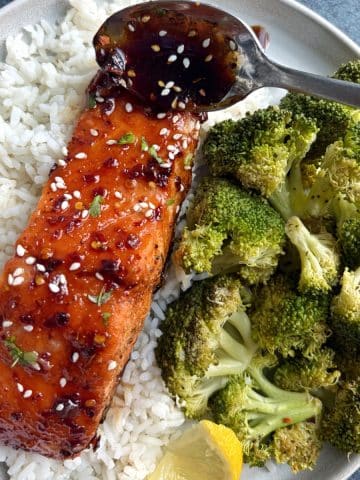 A plate of rice, broccoli, and honey soy salmon with a spoon pouring on more of the sauce on top.
