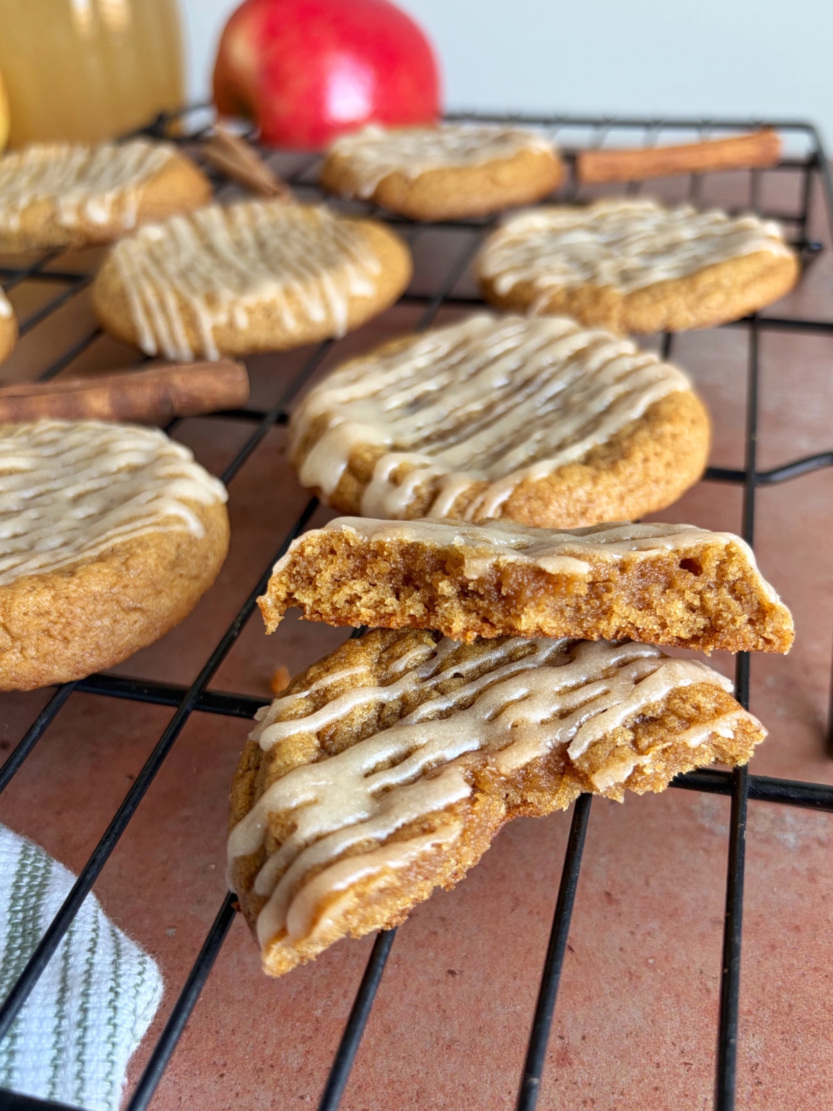 A wire rack filled with apple cider cookies, with the front cookie broken into two to display the inside texture.