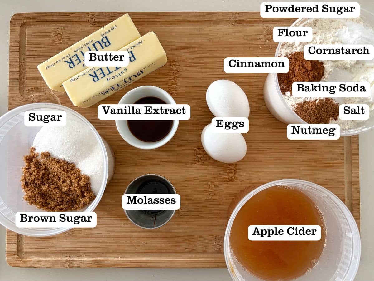 A wooden board with containers of ingredients to make apple cider flavored cookies.