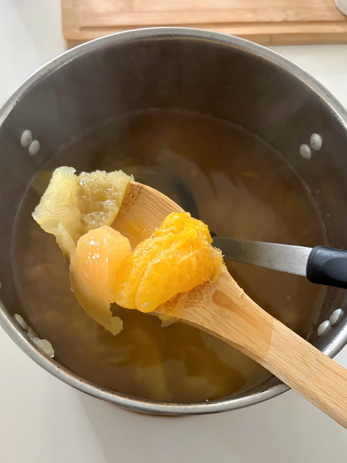 A wooden spoon with boiled fruit held over a silver pot.