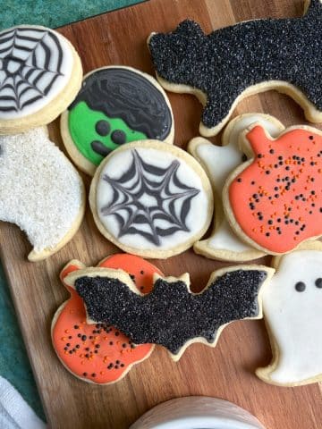 A wooden tray with lots of royal icing-decorated sugar cookies shaped like Halloween designs.