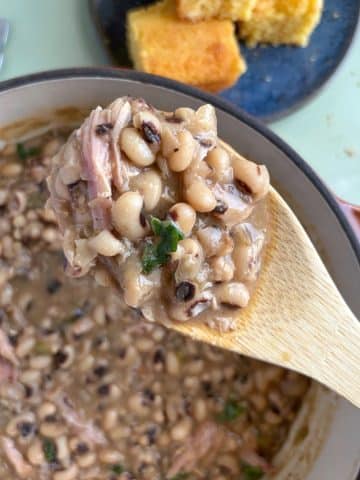 A wooden spoon holding up a serving of black eyed peas over the rest of the pot.