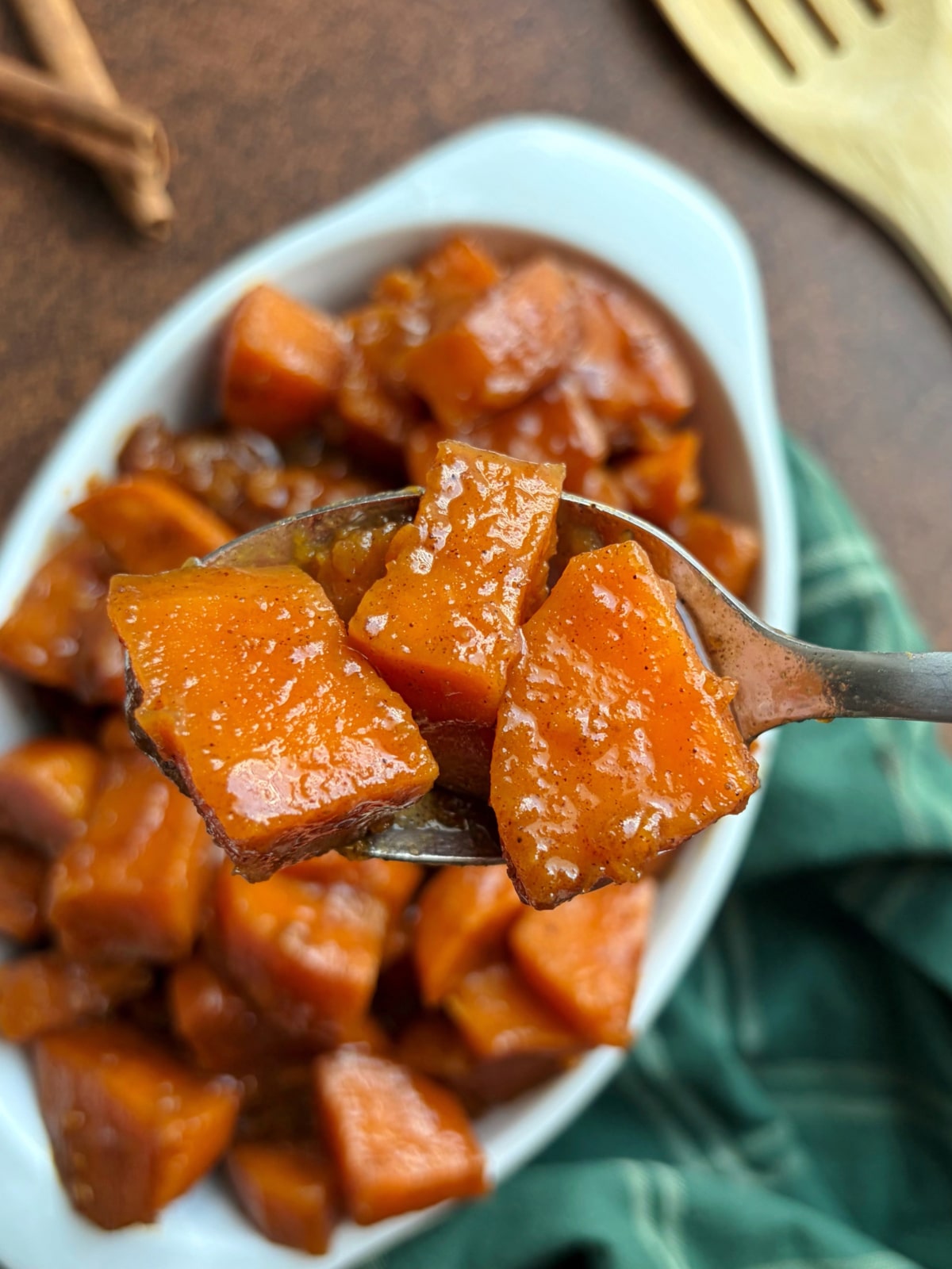 A spoonful of candied yams held above the rest of the batch in a baking dish.
