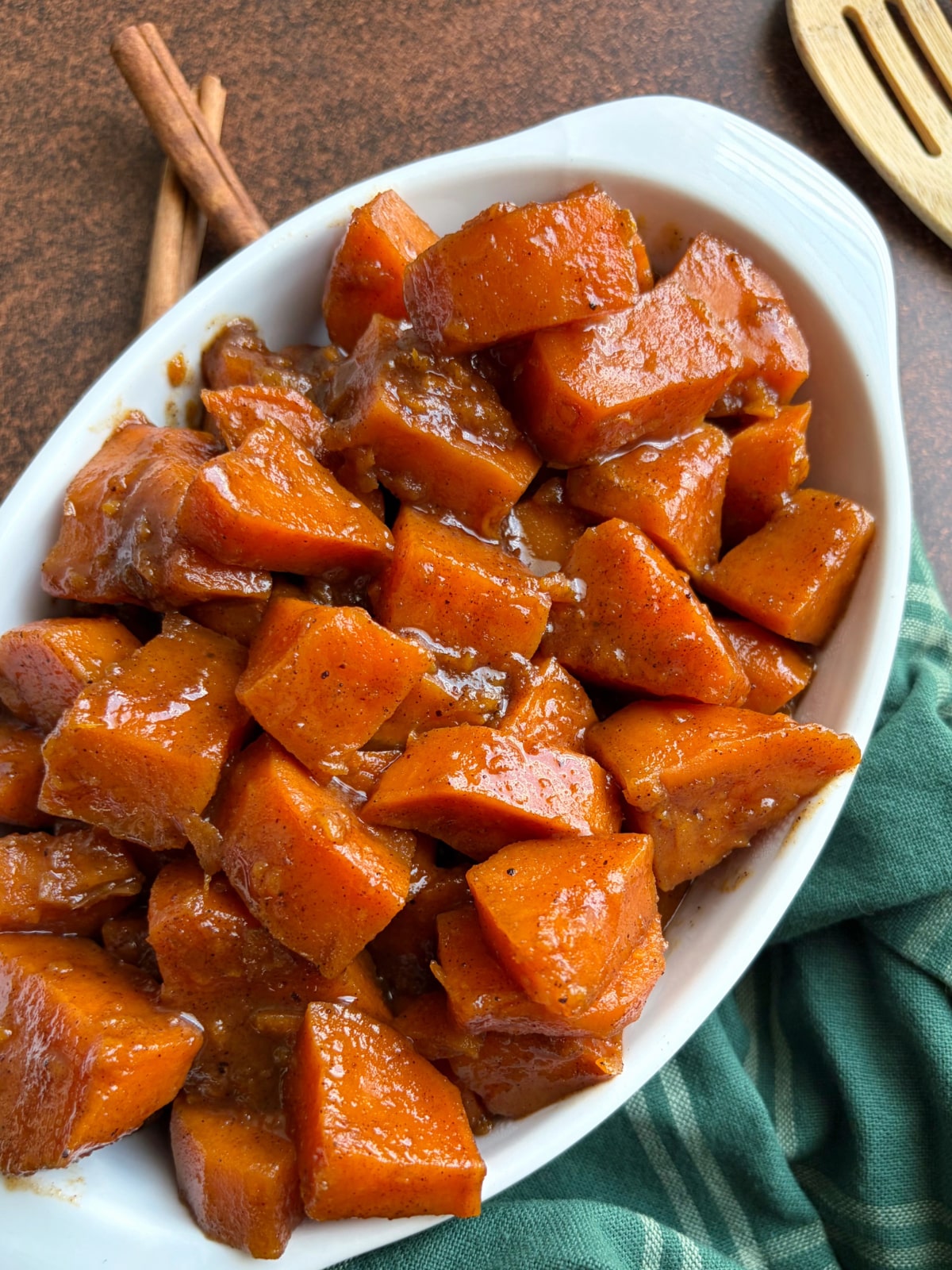 A dish of candied sweet potatoes with cinnamon sticks and a serving utensil on the side.