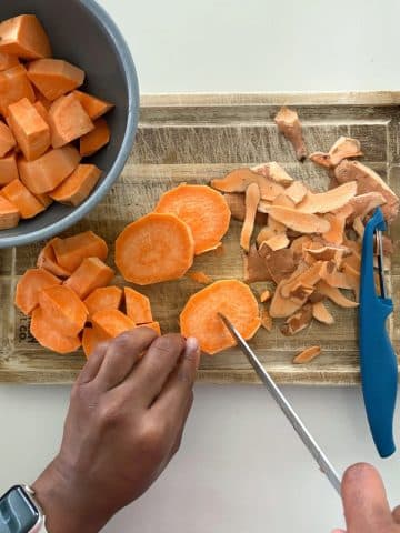A pair of hands cutting up sweet potatoes into quarters on a wooden cutting board.