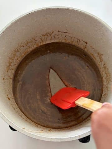 A person dragging a silicone spoon through a brown sugar glaze in the bottom of a pot.